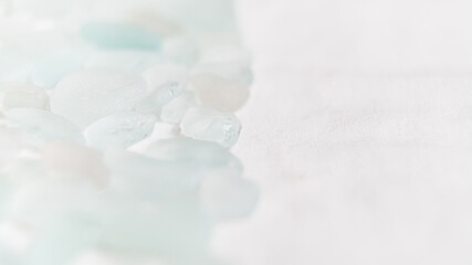 Close-up of pale sea glass pieces on soft white fabric, showcasing delicate texture and serene arrangement. A minimalist composition evoking harmony and subtle beauty