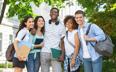 Group of international students posing in front of university, looking at camera and smiling