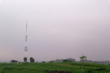 sky with thick, gray clouds looms over a green field. A lone tower stands tall, adding a touch of human presence to the vast landscape.
