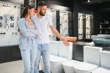 Young couple choosing lavatory pan standing together in the building shop with sanitary ceramics