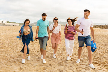 Obraz premium A group of five friends strolls along the sandy beach, chatting and holding drinks. The sun shines brightly as they enjoy their time together, creating a joyful atmosphere.
