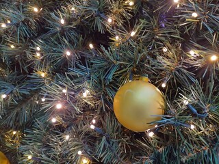 Detail of Christmas tree decoration with golden color scheme. Ball ornaments and at green fir tree. Magic background of christmas decoration in sparkling holiday lights.