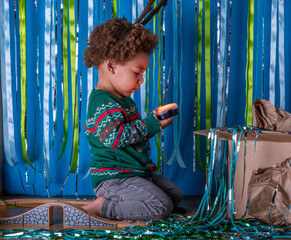 Young toddler, child at looks at a light from a box at Christmastime. Curious boy wearing his festive jumper. Party time.