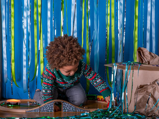 A young ethnic boy plays trains on stage with a glitter, blue and green backdrop.