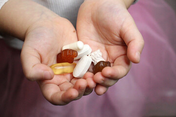 Child holding various pills and supplements in palms.