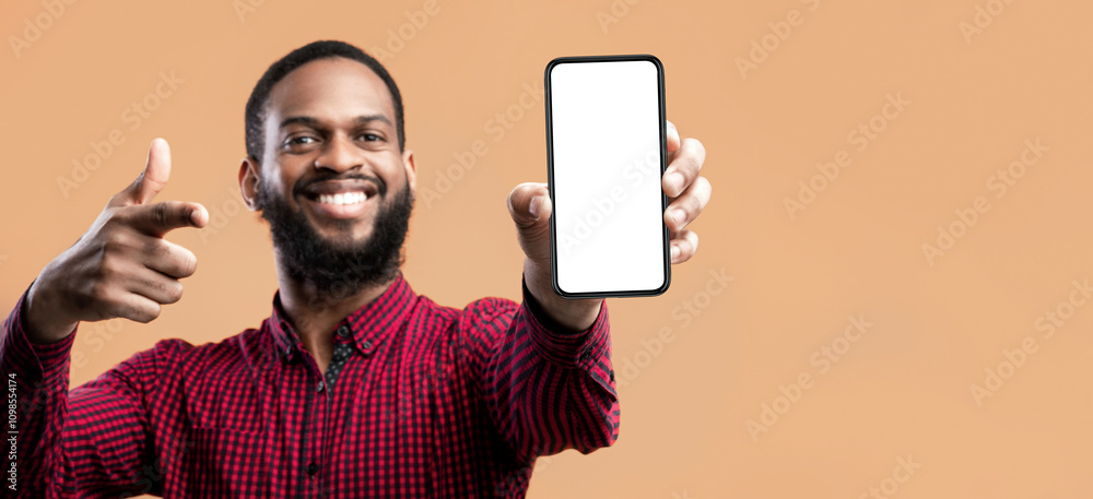 Poster Trendy Mobile Phone. Smiling bearded black man holding latest slim smartphone with white blank screen in hand and pointing at it, indicating empty space for mock up, blurred background
