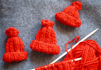 Three small red elf hats, perfect for gnomes, elves, or Santa's helpers, displayed alongside an unfinished knitting project. The scene evokes a festive, whimsical holiday atmosphere