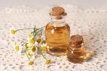 Bottles of essential oil and chamomile flowers on table, closeup