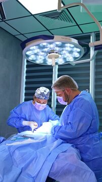 Female surgeon applies different tools at operation on thyroid. Male doctor assists at procedure. . Vertical video.