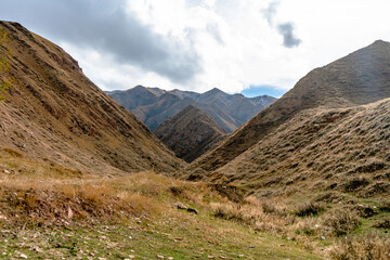 Obraz premium A stunning mountain valley with steep grassy slopes leading to rugged peaks in the distance. The serene landscape under partly cloudy skies highlights the untouched beauty and outdoor wilderness