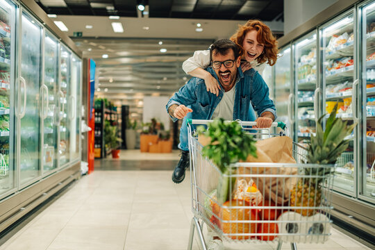 Happy couple having fun riding shopping cart in supermarket