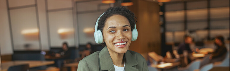 A woman with headphones sitting at a table with coffee and laptop in a nice modern coworking office