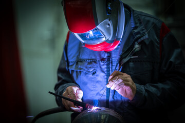 A worker manually welds steel and stainless steel components using TIG technology, detail of an electric arc.