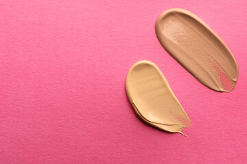 Fototapeta premium Foundation on pink background, top view with space for text. Smears of cosmetic product