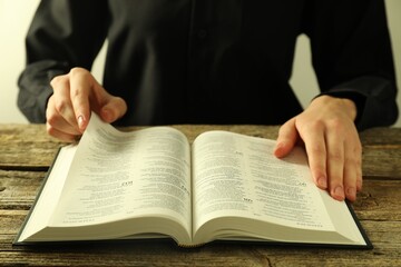 Woman reading Holy Bible in English language at wooden table, closeup