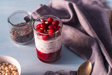 Pudding with cranberries, yegurt, chia seeds and pine nuts on a blue table with a spoon and a gray...