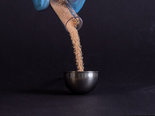 laboratory powder is poured from a glass tube, powder grains fall on a pile of powder on a dark...