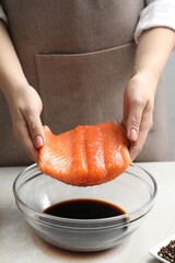 Woman with salmon fillet and soy sauce at gray table, closeup