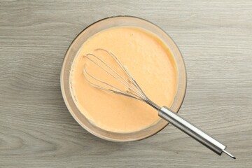 Bowl with dough for pumpkin pancakes and whisk on wooden table, top view