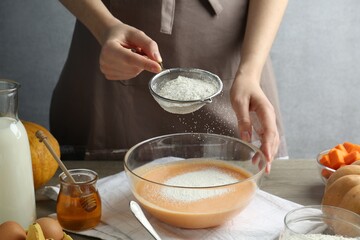 Making pumpkin pancakes. Woman adding flour to dough at table, closeup