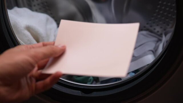 Detail cropped shot of unrecognizable man using laundry detergent sheet to load washing machine with dirty clothes, demonstrating modern and convenient laundry method, close-up, slow motion.