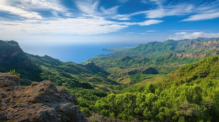 Obraz premium Stunning panoramic view of lush green mountains transitioning into a serene coastline under a bright blue sky with scattered clouds.