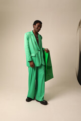 Vertical portrait of young African American man wearing green suit posing over light background. Vertical mock-up.