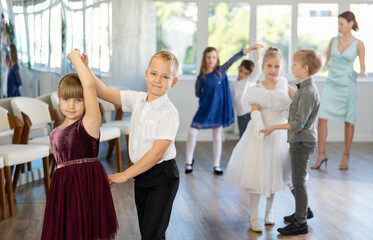 Joyful schoolboys and schoolgirls of primary classes training valse dance in events salon