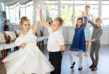 Enthusiastic preteen children, boys and girls in party attire performing elegant waltz in pairs in...