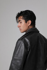 Side portrait of handsome young man wearing biker jacket and posing over white background. Vertical.