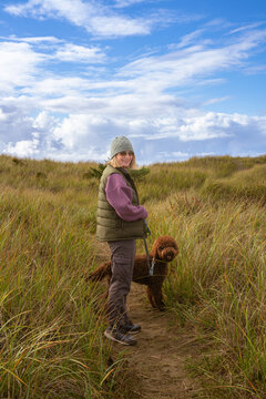 A woman walking her dog through beach grass at Ocean Shores, Washington.