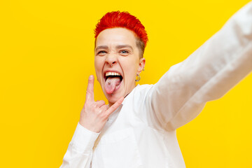 short-haired red-haired punk girl shows rock gesture and makes selfie