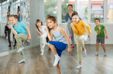 Fototapeta premium Positive juvenile girl engaged in Rock-n-Roll dance together with children's group and female trainer in training room