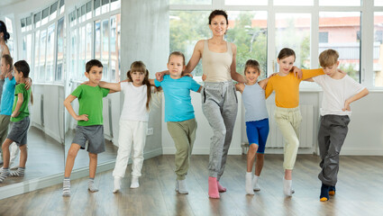 Fototapeta premium Group of children stand in row holding hands, performing Irish folk dance with woman teacher. Studio school for amateur and professional dancers