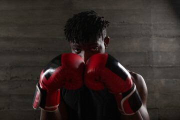 strong confident african american boxer in red gloves stands in a defensive stance near a punching...
