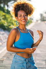 Young woman holding sunglasses is smiling outdoors