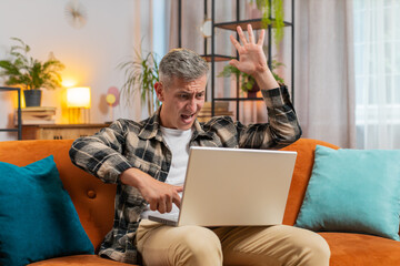 Displeased man with gray hair use laptop notebook working typing, loses becoming surprised sudden...