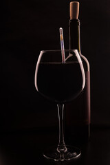 transparent glass goblet with wine and bottle of wine with cork on black background
