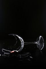 Broken transparent glass goblet with a drop of wine on a black background