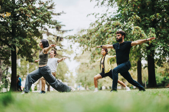 A diverse group of students engages in a yoga class outdoors, guided by a teacher. They perform calm and focused exercises surrounded by lush greenery and a tranquil environment.