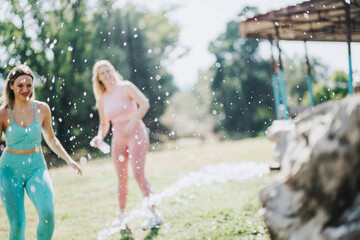 Two friends enjoy playful water activities in a sunny park setting, wearing colorful active wear. The image captures a moment of joy, energy, and relaxation amidst nature.