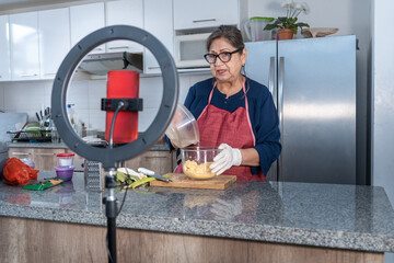 Senior Latina woman recording a video with a light and a red cell phone for social media