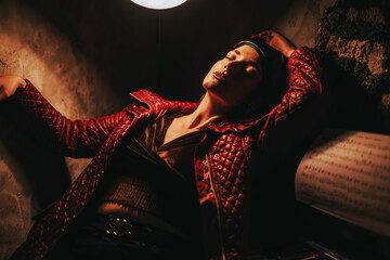 A woman in a red jacket poses dramatically under dim lighting, expressing contemplation and emotion. The intimate setting and play of shadows add depth to the artistic composition. © qunica.com