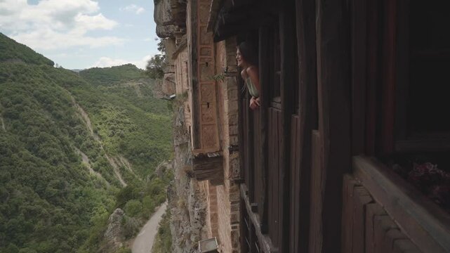 female tourist leans through an open window and smiles while visiting Holy Kipinas Monastery in Greece