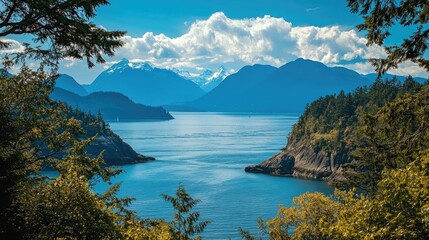 Breathtaking view of tranquil ocean framed by rugged mountains under a vibrant blue sky with scattered clouds and lush greenery.