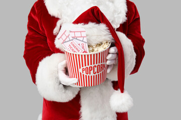 Santa Claus with bucket of popcorn, cinema tickets and hat on grey background. Closeup