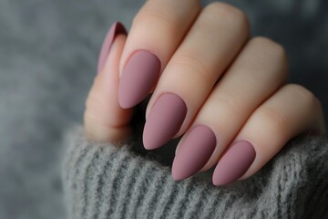 A close-up view of a hand with elegantly shaped, matte mauve nails, resting on a cozy, knitted sweater, showcasing a stylish and chic aesthetic.