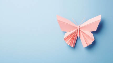 Fototapeta premium A delicate pink paper butterfly displayed against a soft blue background, showcasing creativity and craftsmanship.