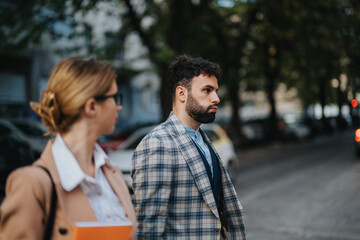 Fototapeta premium A man and woman engaging in a business discussion while walking outdoors in the city. The scene captures professional attire and an urban background, emphasizing modern business communication.