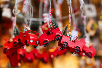 Red metal toy cars adorned with small green Christmas trees are hanging as festive ornaments. These decorations capture nostalgic holiday feel, perfect for adding charm to Christmas tree